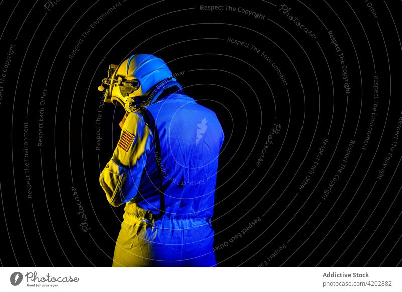Astronaut im Raumanzug in blauem und gelbem Neonlicht stehend Mann Schutzhelm professionell Kosmonaut schützend Panzerung Raumfahrer Missionsstation neonfarbig