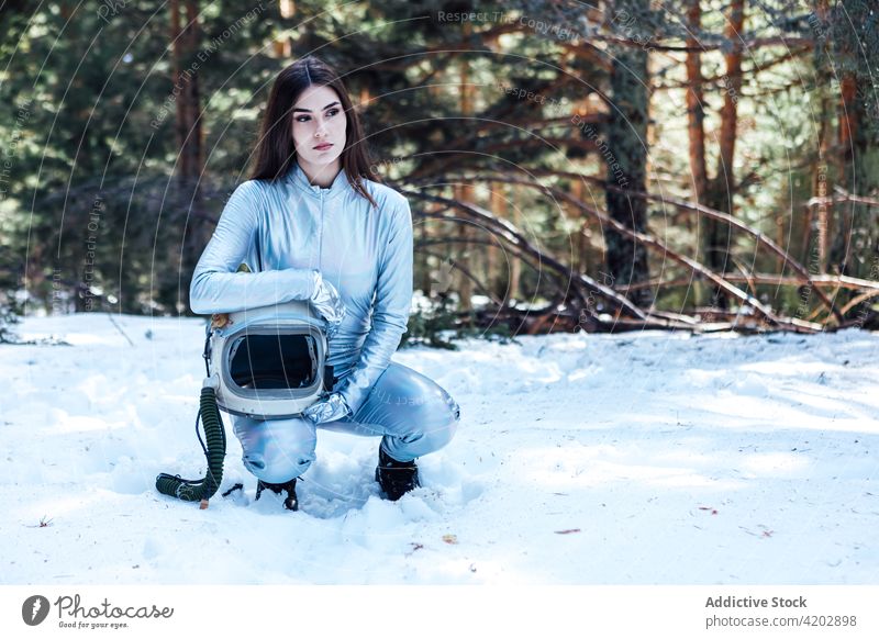 Attraktive Astronautin hockt im verschneiten Wald Frau Schnee Kosmonaut Raumanzug Windstille Winter Astronomie Schutzhelm Entdecker emotionslos professionell