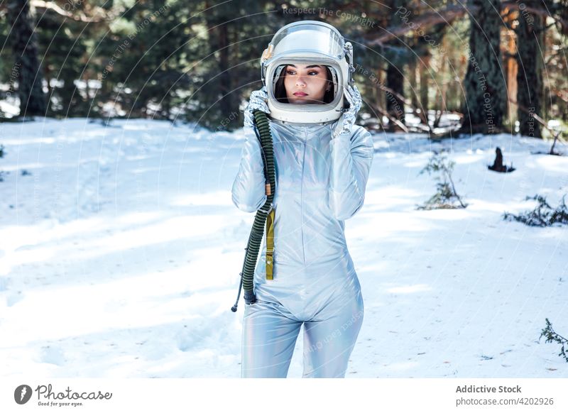 Entschlossene Frau mit Weltraumhelm in verschneitem Wald stehend Astronaut Raumanzug ernst Schnee Raumfahrerin Kosmonaut Winter Astronomie Schönheit Schutzhelm