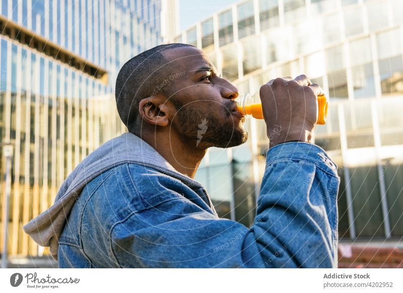 Schwarzer Mann trinkt köstliches Getränk auf einer Straße in der Stadt trinken Saft Erfrischung Flasche genießen nachdenken maskulin Großstadt Porträt