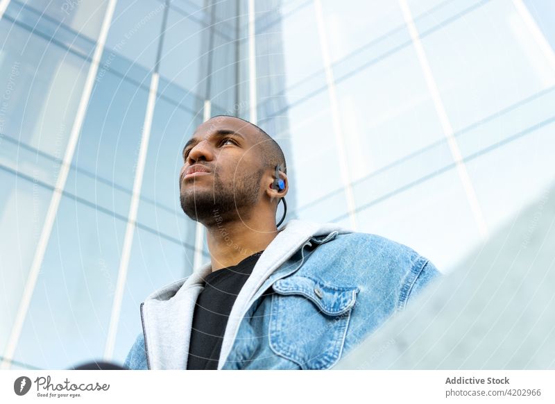 Schwarzer Mann hört Musik über Kopfhörer in der Stadt zuhören Drahtlos Gesang verträumt maskulin Porträt benutzend Gerät Macho brutal Gebäude modern Straße