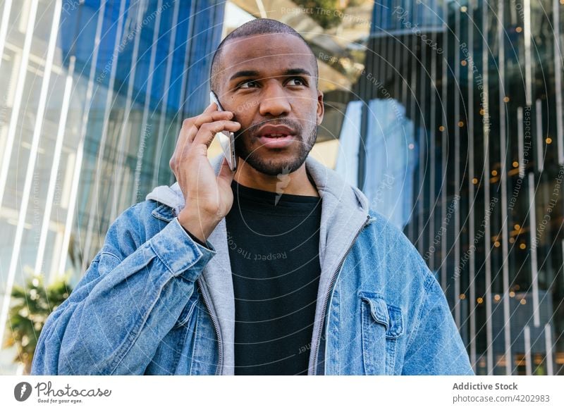Maskuliner schwarzer Mann, der auf einer Straße in der Stadt mit einem Smartphone spricht sprechen maskulin brutal Macho Telefonanruf Großstadt Porträt