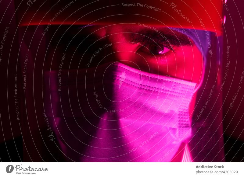 Männlicher Arzt mit Maske in einem dunklen Raum mit rotem Neonlicht Chirurg Mann Mundschutz medizinisch dunkel neonfarbig Licht Medizin behüten leuchten steril