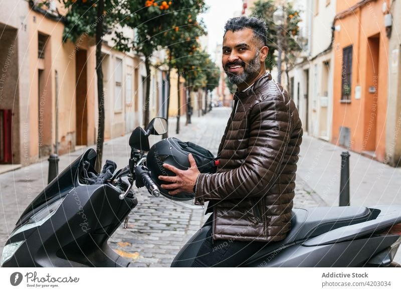 Lächelnder ethnischer Biker auf modernem Motorrad auf einer Stadtstraße Motorradfahrer Fahrrad maskulin brutal viril Macho Mann Großstadt Porträt Inhalt