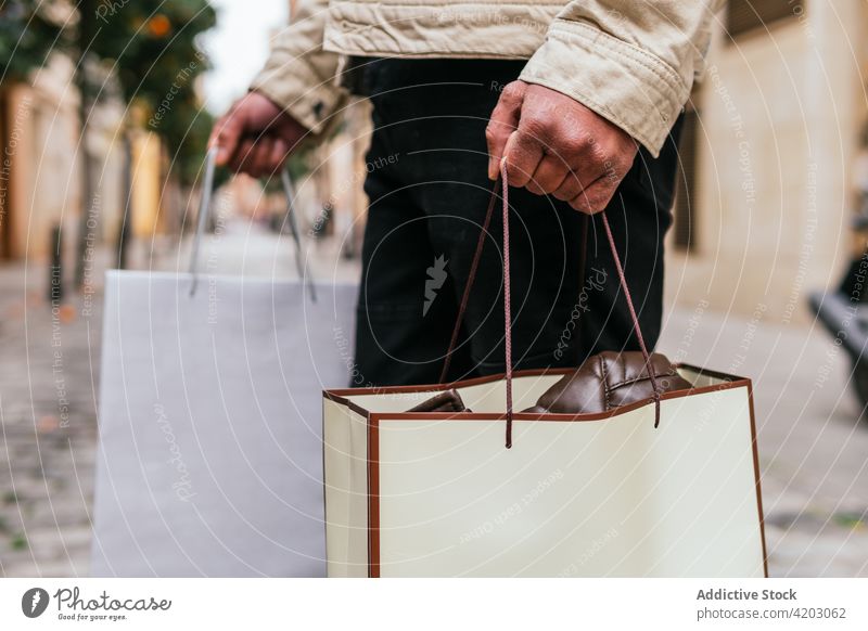Männlicher Hopper mit Geschenktüten auf einer Stadtstraße Käufer Einkaufstasche Straße maskulin Spaziergang Stil Mann urban Lifestyle präsentieren Überraschung
