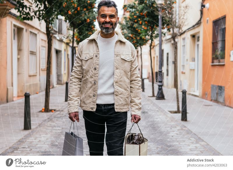 Lächelnde hispanische Käuferin mit Geschenktüten auf einer Stadtstraße Einkaufstasche Straße maskulin Spaziergang Stil Mann urban Lifestyle ethnisch froh