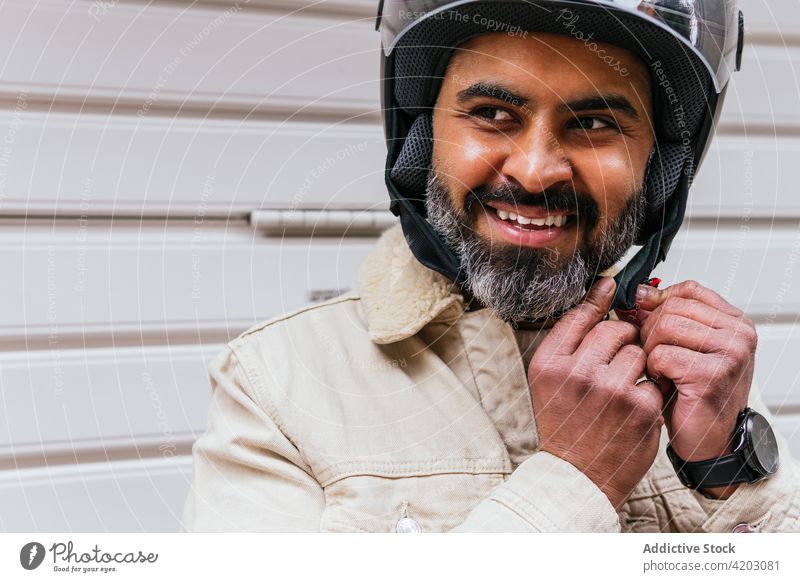 Lächelnder hispanischer Motorradfahrer beim Aufsetzen des Helms auf der Straße Biker angezogen Schutzhelm heiter brutal maskulin viril Mann Porträt freundlich
