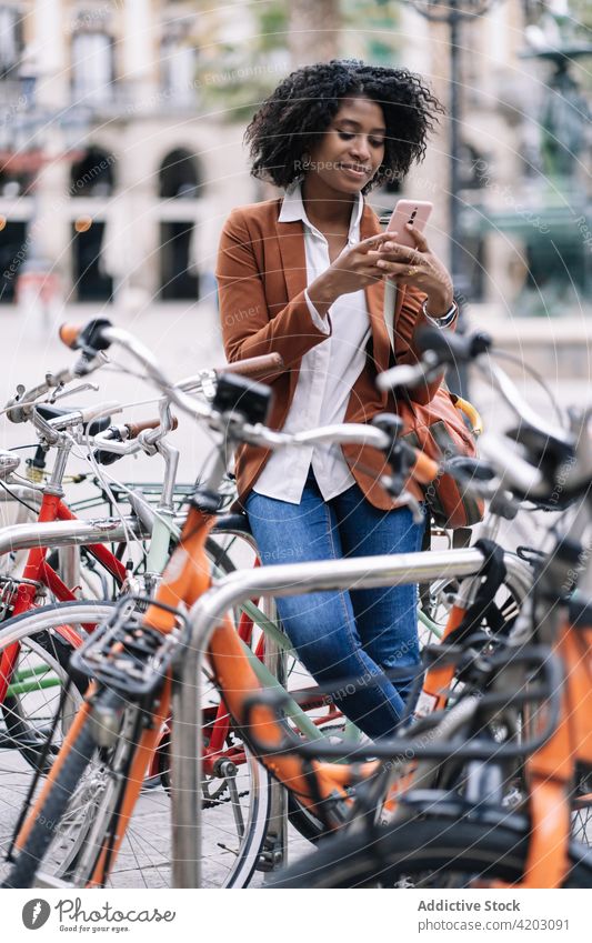 Schwarze Frau durchsucht Smartphone in der Nähe des Fahrrads Browsen zuschauend sprechen Großstadt geparkt Mobile Telefon heiter schwarz Afroamerikaner ethnisch