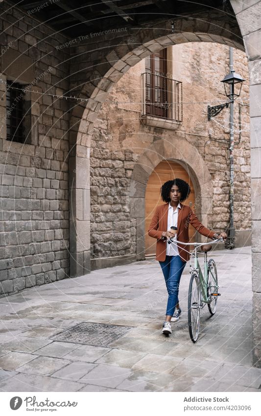 Ethnische Frau geht mit Fahrrad die Straße entlang Arbeitsweg Großstadt Spaziergang trendy schwarz Afroamerikaner ethnisch urban Zeitgenosse Fahrzeug Stadt