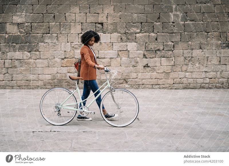 Ethnische Frau geht mit Fahrrad die Straße entlang Arbeitsweg Großstadt smart lässig Spaziergang trendy Stil schwarz Afroamerikaner ethnisch urban Zeitgenosse
