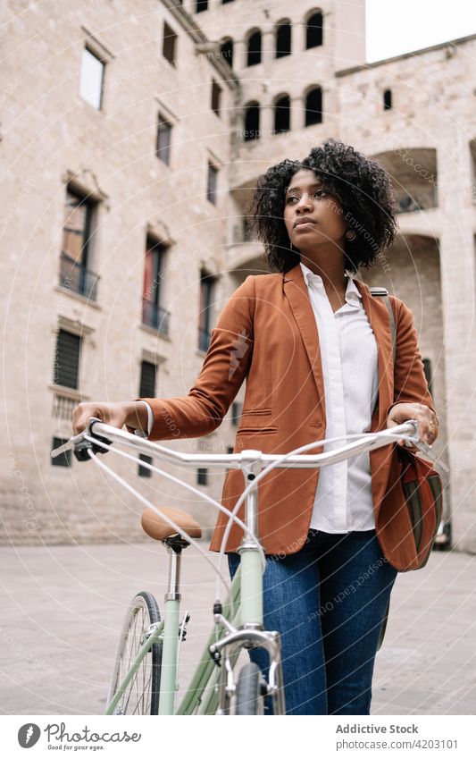 Ethnische Frau geht mit Fahrrad die Straße entlang Arbeitsweg Großstadt smart lässig Spaziergang trendy Stil schwarz Afroamerikaner ethnisch urban Zeitgenosse