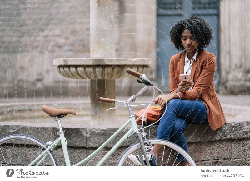 Junge schwarze Frau mit Fahrrad und Smartphone auf der Straße benutzend urban Mobile Browsen Telefon online jung Afroamerikaner Schüler tausendjährig Apparatur