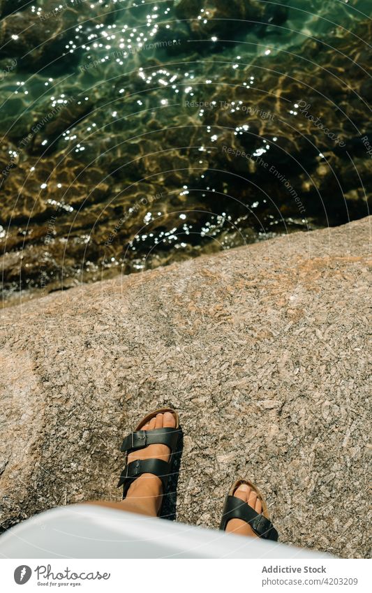 Nahaufnahme von Frauensandalen auf einigen Felsen und dem Meer darunter Fuß Sandalen Steine Strand Sommer Hintergrund abschließen Schuhe Mädchen reisen weiß