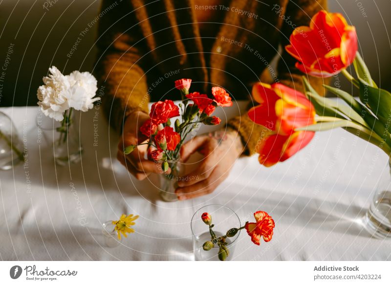 Mann mit Blumensträußen aus frischen, hellen Blumen am Tisch sitzend Blumenhändler Blütezeit Nelke Tulpe Glaswaren Feiertag Blumenstrauß männlich geblümt