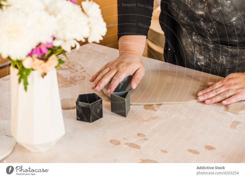 Anonyme Kunsthandwerkerin formt Ton mit geometrischen Formen Frau Werkstatt Hobby Fähigkeit geschnitten Figur Formular Handwerkerin Schürze lässig schwarz Tisch