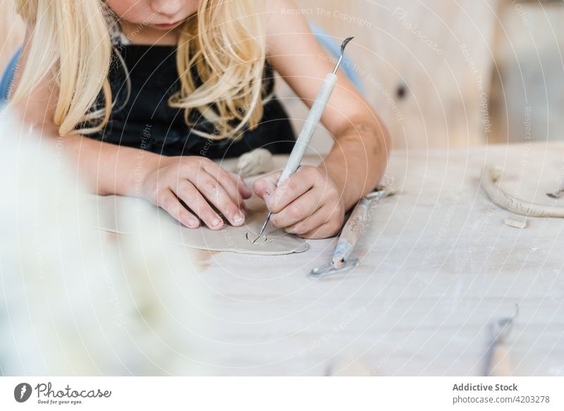 Unerkanntes Kind schneidet Tonstück im Atelier Mädchen Töpferwaren Spielfigur geschnitten Öhr Hobby Werkstatt Instrument Handwerk schwarz Schürze Tisch stechend