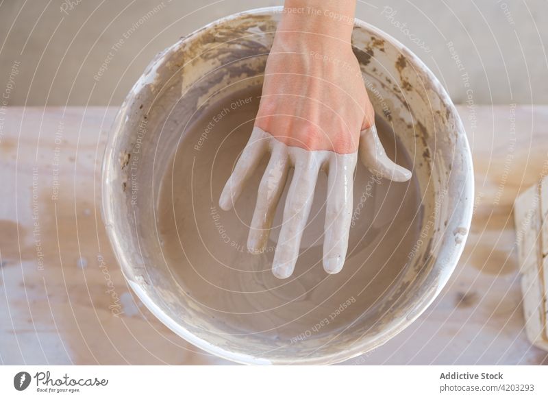 Gesichtsloser Kunsthandwerker, der eine Hand in Ton aus einem Eimer in der Werkstatt zieht Frau ziehen Hobby Töpferwaren Handwerkerin Kleinunternehmen Prozess