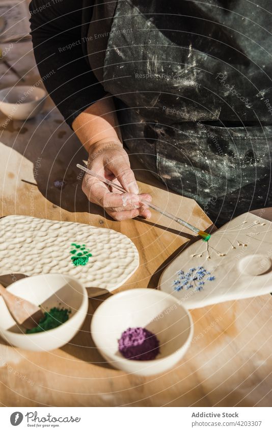 Unbekannte Frau, die mit einem Pinsel auf ein Brett zeichnet Hobby keramisches Pigment Bürste Zeichnung Palette Kunst Werkstatt Pinselblume Handwerkerin Prozess