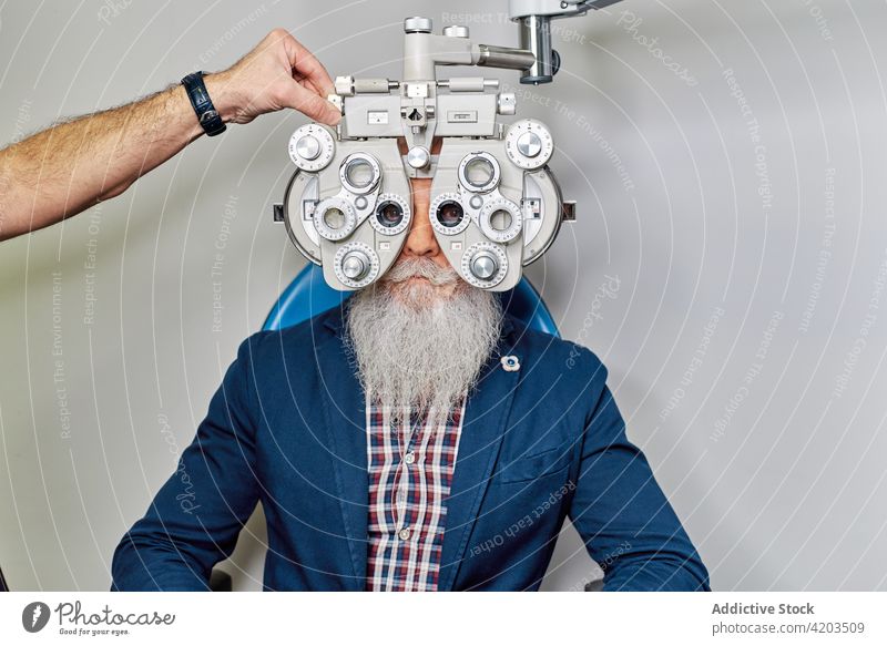 Optometrist mit Phoropter bei der Augenuntersuchung Augenoptikerin Augenlicht Diagnostik Optiker Ophthalmologie Optometrie untersuchen geduldig Senior männlich