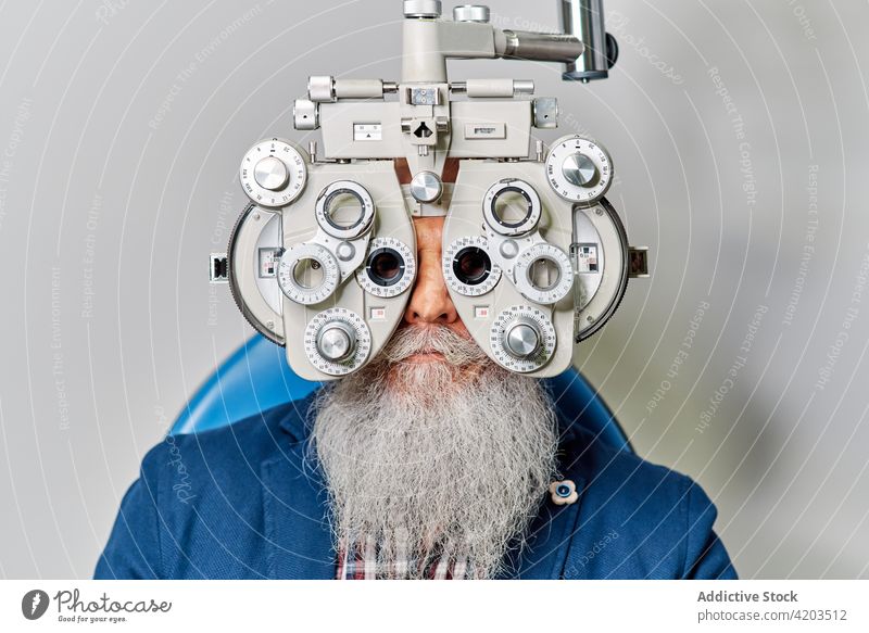 Älterer Mann mit Phoropter bei der Augenuntersuchung Augenoptikerin Augenlicht Diagnostik Optiker Ophthalmologie Optometrie untersuchen geduldig Senior männlich