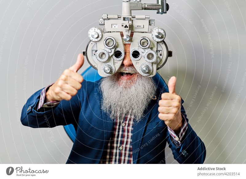 Älterer Mann mit Phoropter bei der Augenuntersuchung Augenoptikerin Augenlicht Diagnostik Optiker Ophthalmologie Optometrie untersuchen geduldig Senior Arzt