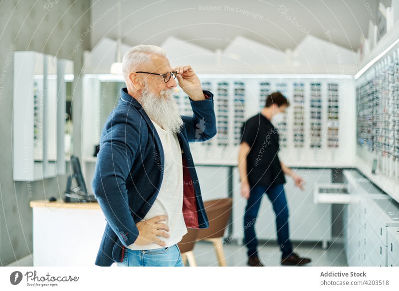 Optiker hilft einem älteren Mann bei der Auswahl einer Brille in einem Optikgeschäft Hilfsbereitschaft optisch Laden wählen Senior angezogen Kunde Dienst