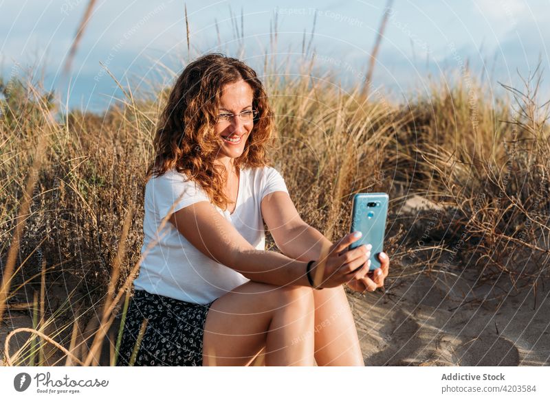 Frau nimmt Selfie am Strand bei Sonnenuntergang Smartphone Browsen Sommer Inhalt benutzend Ufer Sand Outfit Mobile Apparatur Abend Urlaub Wochenende ruhig