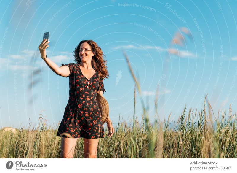 Lächelnde Frau nimmt Selfie auf Smartphone in der Natur Sommer Feld Kleid Sonnenuntergang Selbstportrait Moment Gedächtnis fotografieren genießen Apparatur