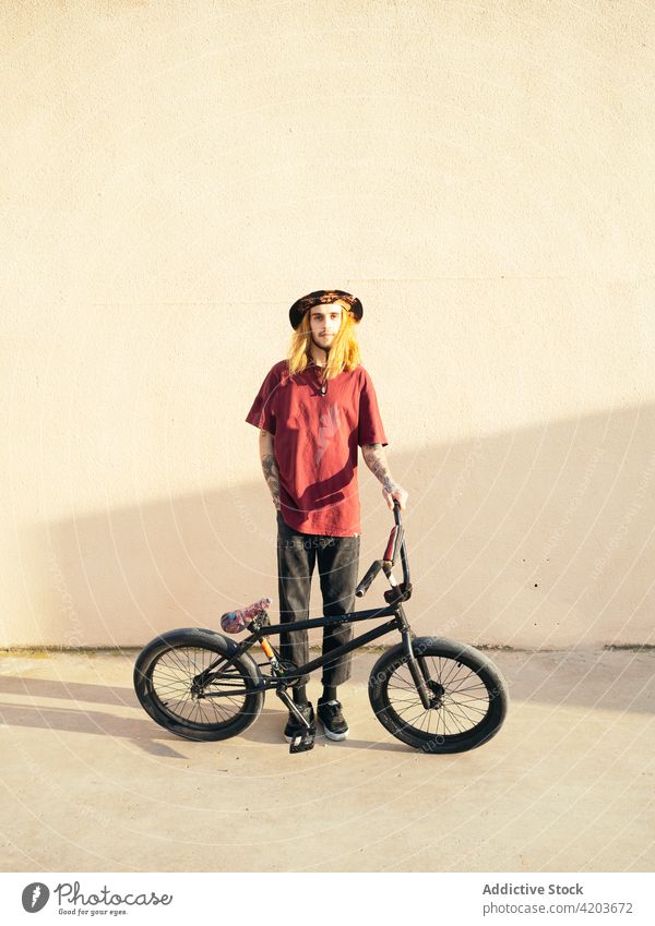 Tätowierter Biker mit BMX-Fahrrad auf dem Bürgersteig Testversion Hipster bmx Sport Individualität cool Hand-in-Tasche Mann Straßenbelag modern Stil kreativ