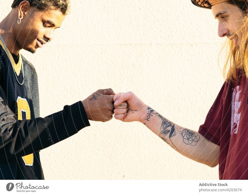Crop multiethnische männliche Freunde schlagen Fäuste im Sonnenlicht Fistbump Gruß Tattoo cool Lächeln Zeit verbringen Wochenende Männer Porträt Profil Inhalt