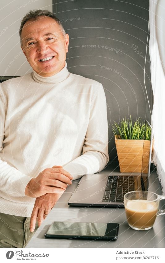 Fröhlicher reifer Mann am Tresen mit Laptop in der Küche stehend Morgen Lächeln heimwärts Frühstück Kaffee Abfertigungsschalter männlich fettarm Tasse Netbook