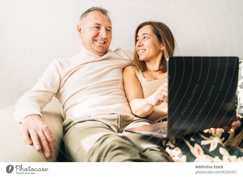 Zufriedenes Paar sieht sich zu Hause einen Film auf dem Laptop an zuschauen kuscheln Sofa heimwärts Wochenende Lebensmitte Wohnzimmer heiter Zusammensein