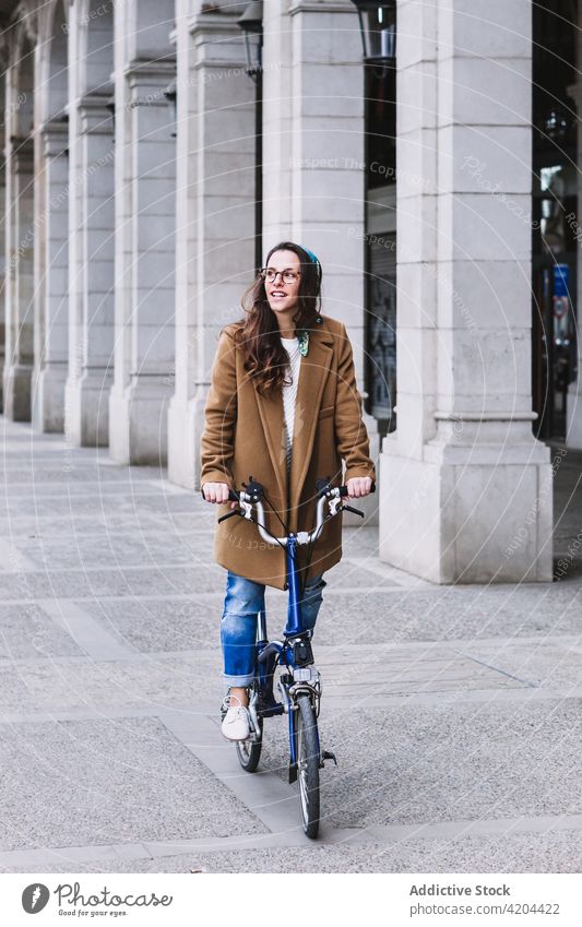 Lächelnde Radfahrerin auf dem Fahrrad auf einer Stadtstraße Biker Kolonnade Architektur Wochenende freie Zeit Frau Straße Großstadt Verkehr heiter genießen