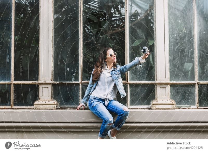 Stilvolle Frau nimmt Selfie auf Fotokamera in der Stadt Fotoapparat Moment Gedächtnis cool Orangerie Fenster benutzend Gerät Jeansstoff Bekleidung Sonnenbrille