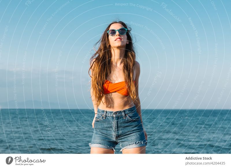Hipster-Frau mit Sonnenbrille am Strand stehend Sommer Stil MEER Outfit trendy Mode jung Brille Accessoire Jeanshose Lifestyle selbstbewusst Teenager Dame Meer