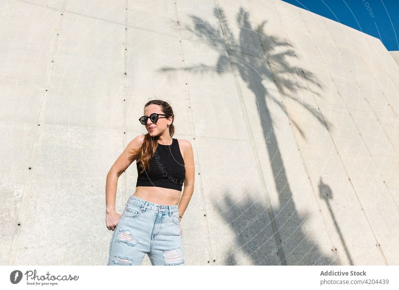 Junge Frau in trendigem Sommeroutfit Stil Outfit Sonnenbrille trendy Mode modern tropisch lässig jung Brille Accessoire Jeanshose Top Handfläche Lifestyle Dame