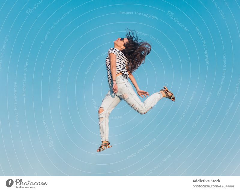 Hipster-Frau in trendigem Outfit springt gegen blauen Himmel Sommer Stil springen Blauer Himmel Sonnenbrille trendy Mode sorgenfrei Streifen Energie Fliege