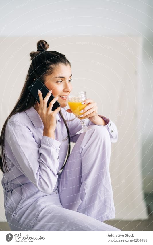 Charmante Frau mit Getränk auf Smartphone zu Hause Saft Moment freundlich charmant heimwärts benutzend Apparatur Gerät orange frisch Glas Erfrischung sprechen