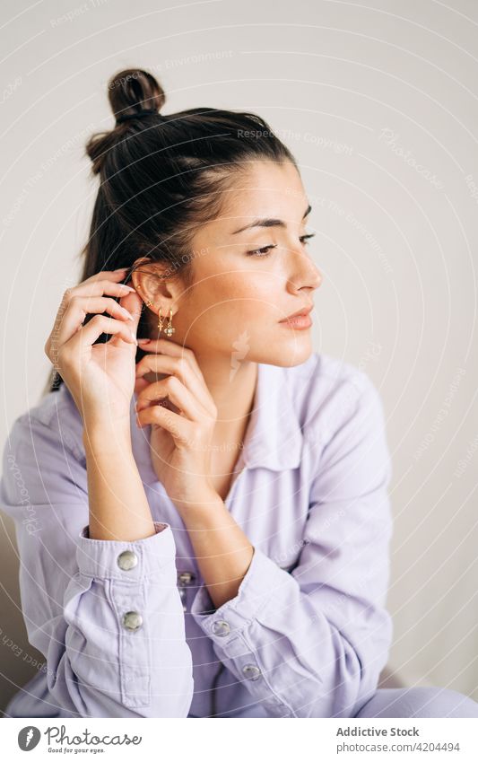 Junge Frau berührt Ohrring auf hellem Hintergrund Ohrringe feminin charmant romantisch verträumt genießen Porträt Accessoire kreativ Design modern Stil zeigen