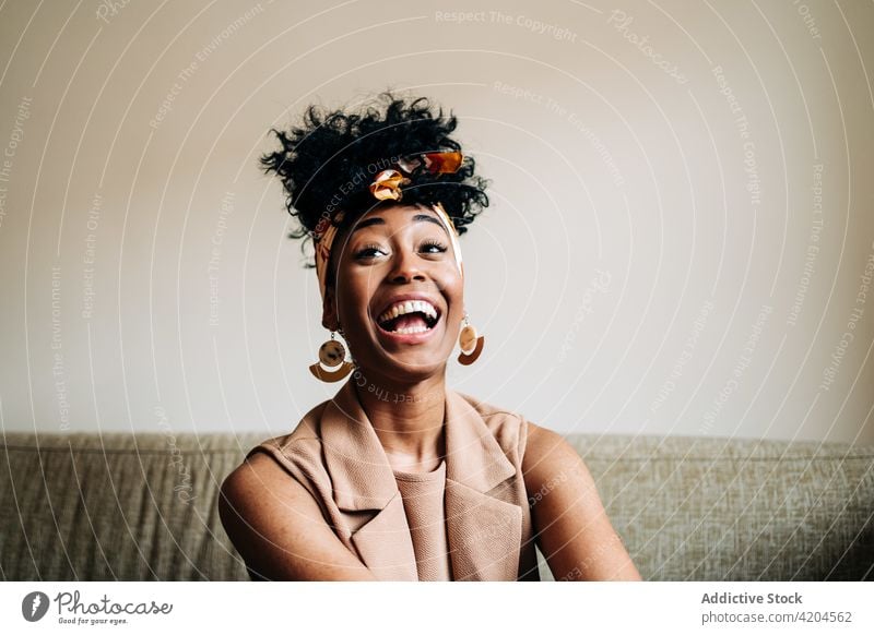 Gelassene schwarze Frau sitzt auf dem Sofa und schaut weg heimwärts Afro-Look heiter Frisur Zahnfarbenes Lächeln heimisch Glück Gelassenheit Windstille ethnisch