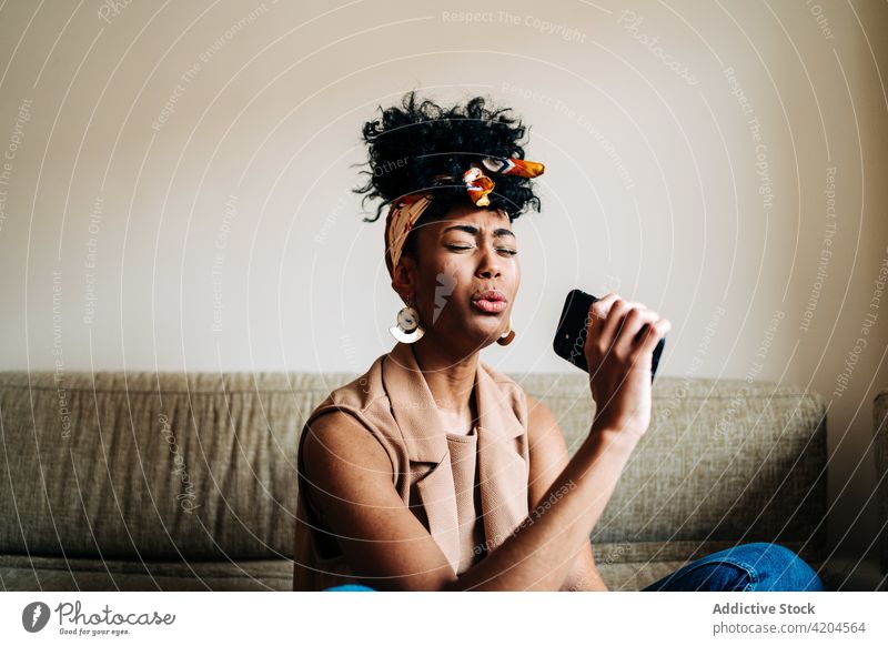 Schwarze Frau singt zu Hause auf ihrem Smartphone singen genießen Gesang Musik kreativ Mikrofon so tun, als ob ethnisch schwarz Afroamerikaner Favorit Sofa