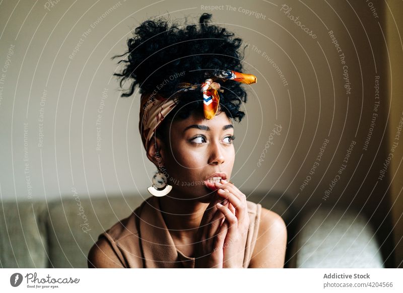 Gelassene schwarze Frau sitzt auf dem Sofa und schaut weg heimwärts Afro-Look Frisur heimisch Gelassenheit sich auf die Hand lehnen Windstille ethnisch