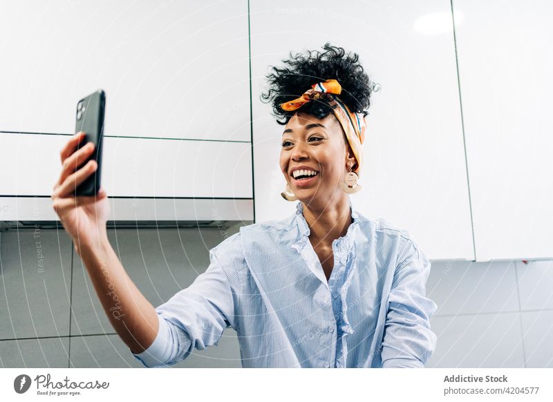 Inhalt ethnische Frau nimmt Selfie in der Küche zu Hause heimwärts heiter Selbstportrait Hausfrau positiv Smartphone Stirnband schwarz Afroamerikaner benutzend
