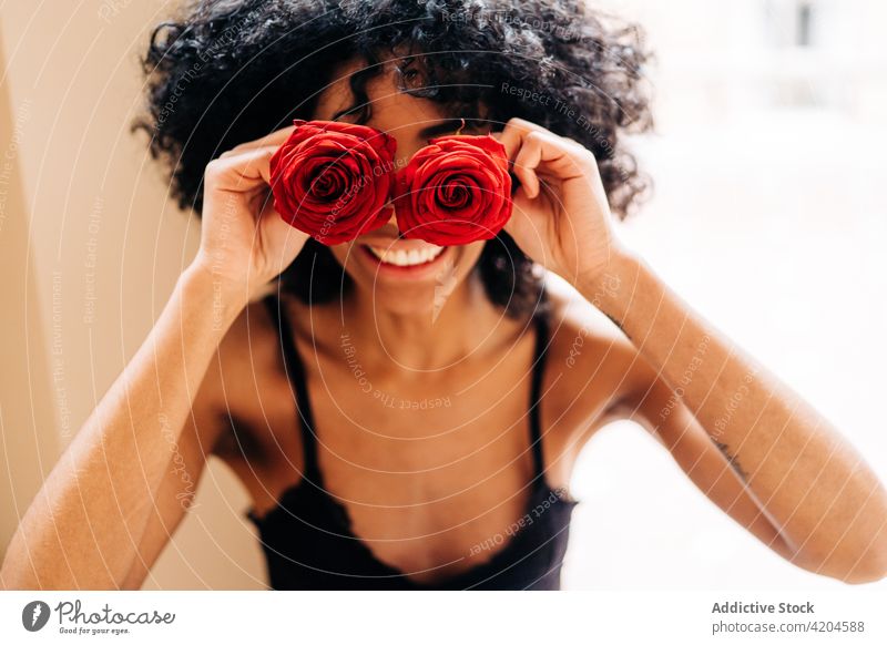 Entzückte schwarze Frau mit Rosenblüten Roséwein Blume Augen abdecken Tierhaut Spaß haben rot Blütenknospen romantisch heiter ethnisch Afroamerikaner Afro-Look