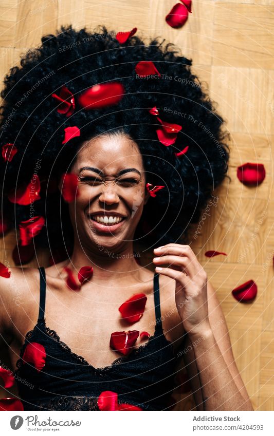 Glückliche schwarze Frau auf dem Boden bedeckt Rosenblättern Herz gestikulieren Liebe Roséwein Blütenblatt romantisch Valentinsgruß Angebot ethnisch
