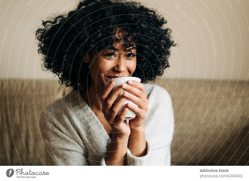 Glückliche schwarze Frau sitzt auf dem Sofa und schaut in die Kamera heimwärts heiter Afro-Look Frisur Gelassenheit Windstille ethnisch Afroamerikaner froh