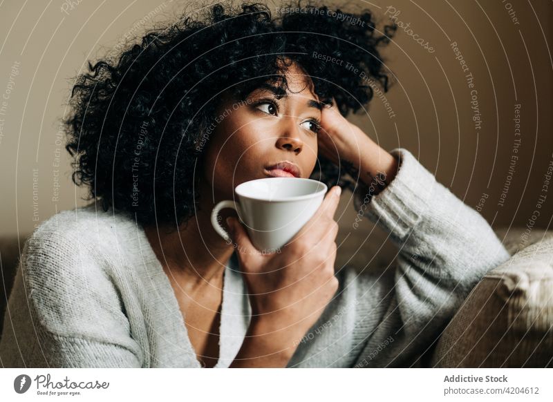 Nachdenkliche schwarze Frau mit Tasse und Getränk schaut weg nachdenklich nachdenken trinken heimwärts allein Melancholie einsam ethnisch Afroamerikaner Becher