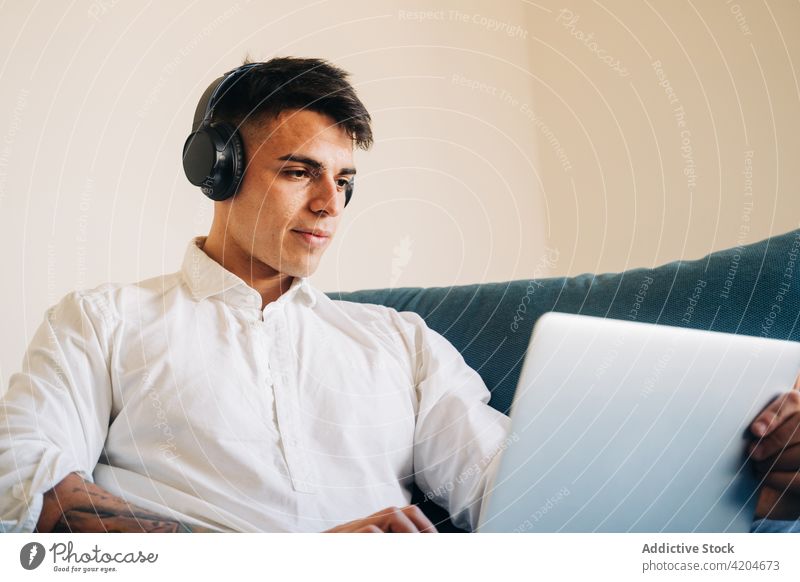 Konzentrierter Mann mit Kopfhörern beim Surfen am Laptop Browsen Internet Liege Netbook online Musik abgelegen Apparatur zuhören Sofa Gerät heimwärts