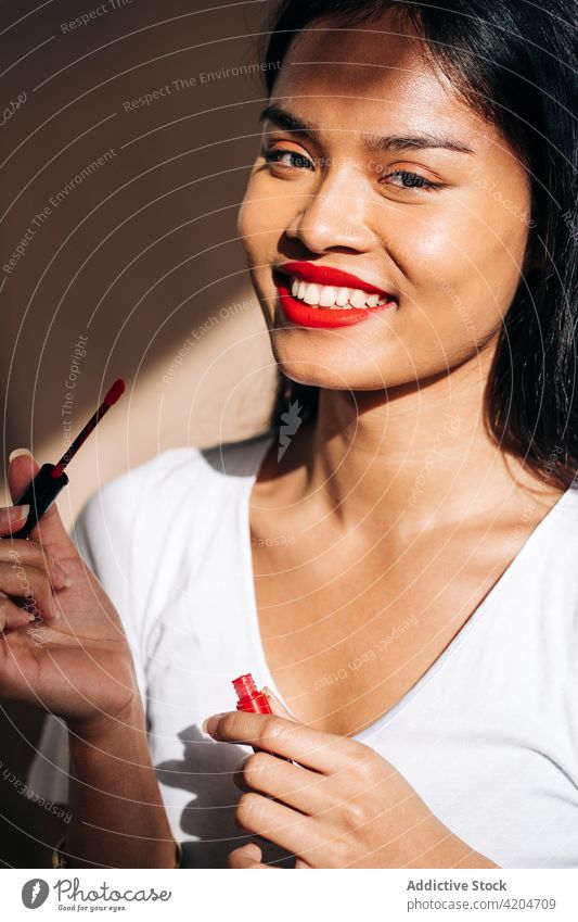 glückliche Frau mit Make-up Lippen färben Lächeln rote Lippen heiter Rouge bewerben Lippenstift Porträt Glück Kosmetik froh dunkles Haar Vorschein
