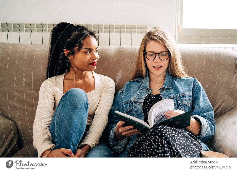 Nachdenkliche Frauen auf dem Sofa, die ein Buch lesen sich[Akk] entspannen ruhen wehmütig Zeit verbringen Roman nachdenklich nachdenken rassenübergreifend